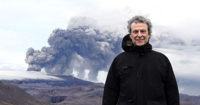 Dr. Jesse Byock, professor of Old Norse and Medieval Scandinavian Studies, with an erupting volcano behind him.